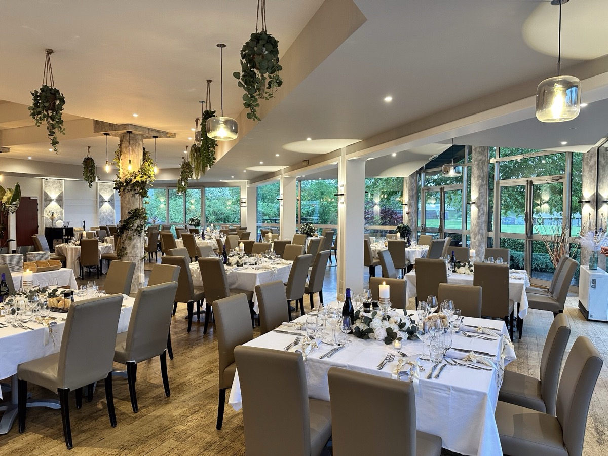 Salle dressée pour un banquet, tables nappées de blanc et vue sur le parc au crépuscule