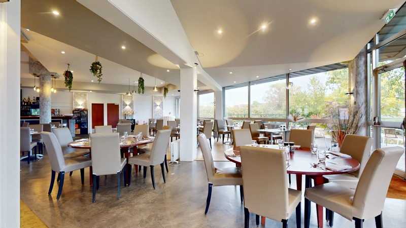 Salle du restaurant avec de grandes baies vitrées ouvertes sur la verdure du parcours de golf