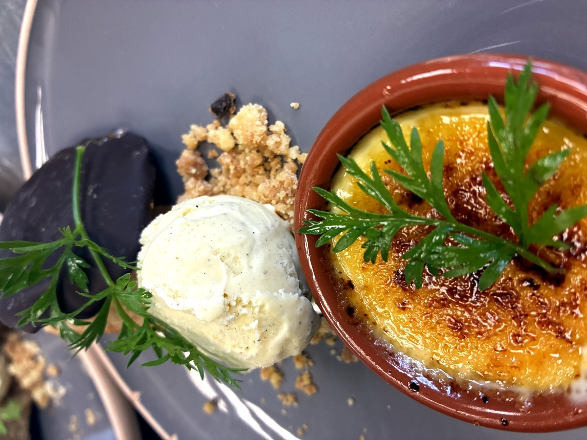 Crème brûlée caramélisée servie avec une glace vanille et une tuile de chocolat