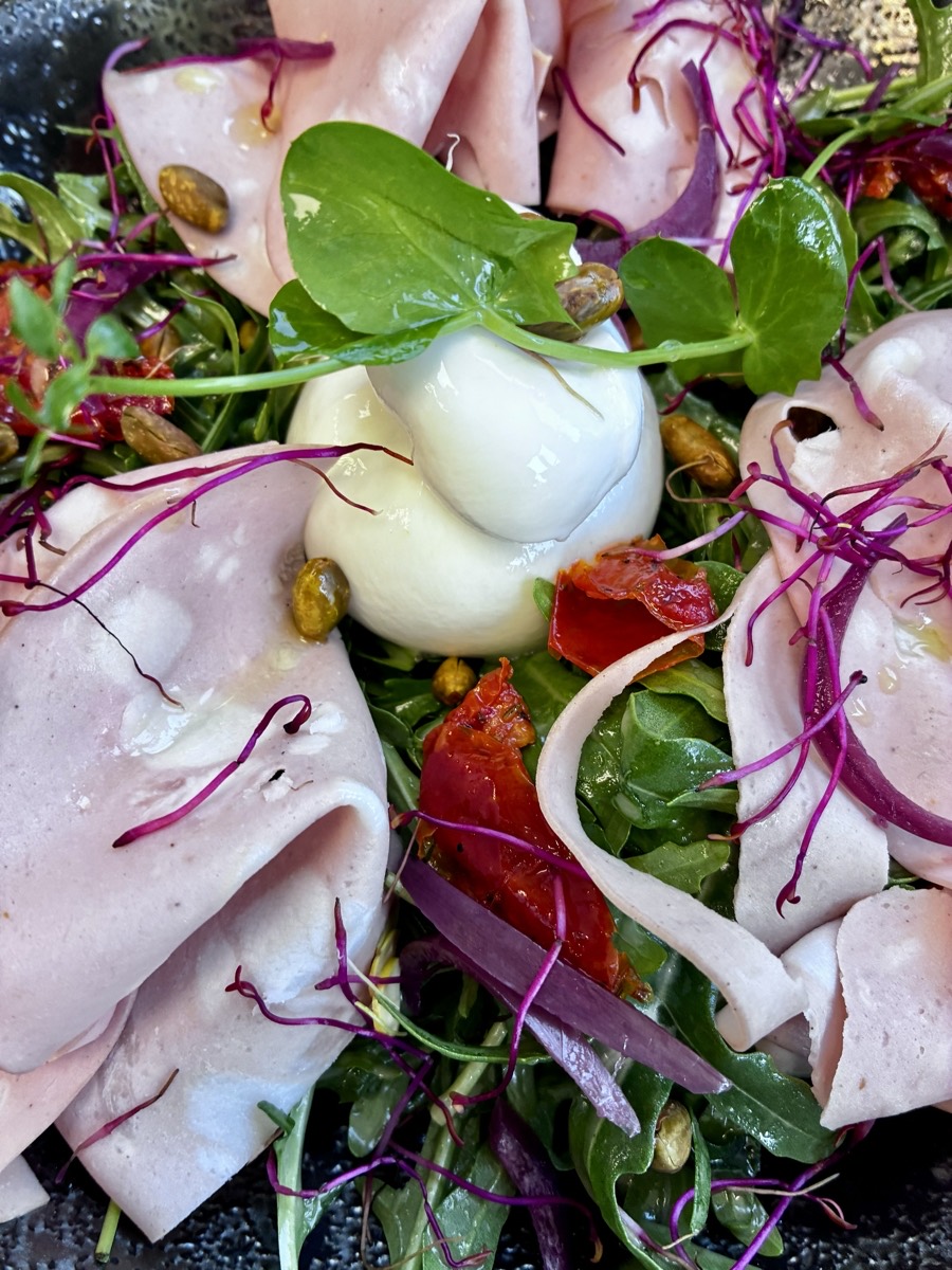 Stracciatella crémeuse, mortadelle, pistaches et tomates confites sur un lit de roquette