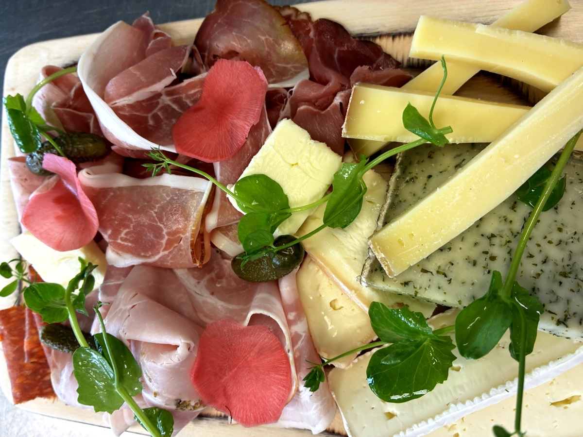 Planche de charcuteries fines et de fromages : jambon sec, mortadelle, brie, comté et bleu, avec cornichons et radis