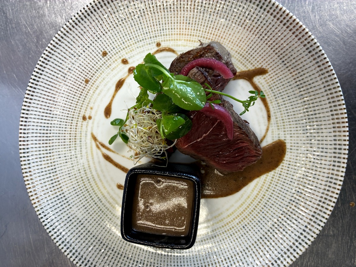 Pièce de rumsteak charolais tranchée saignante, oignons rouges confits, jeunes pousses et sauce servie à part